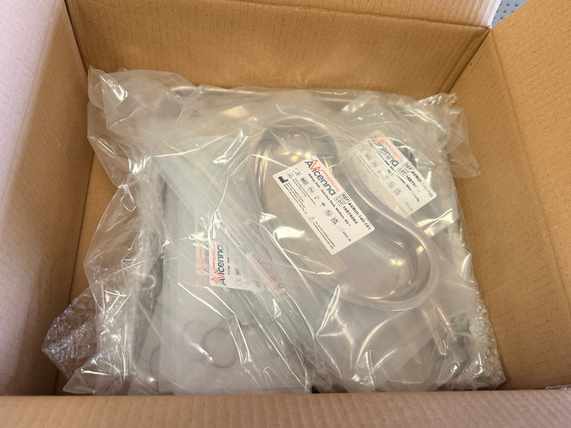 A packaged metal appliance part, likely a dishwasher component, sealed in clear plastic with a printed label, sitting inside an open brown cardboard box.