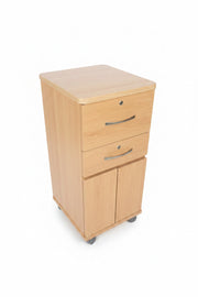 A light wood three-door cabinet with curved silver handles, photographed in a cluttered warehouse or workshop environment with concrete floors and other items in the background.
