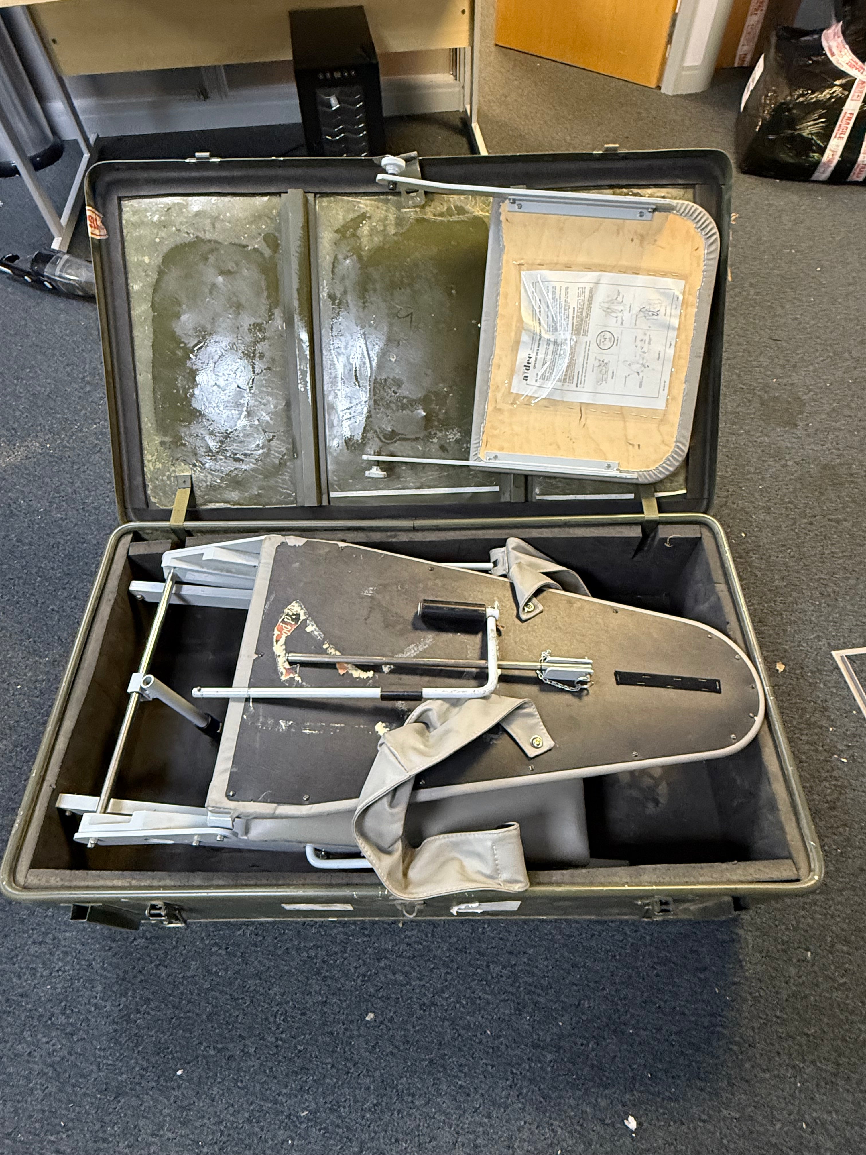 Open suitcase containing a metal chair and documents on a dark surface
