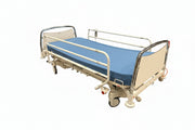An adjustable hospital bed with a blue mattress, beige side panels, and silver metal rails, shown on a plain white background.