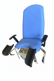 A blue medical examination chair with black armrests and footrests, photographed in a warehouse or storage area with concrete floors and other equipment visible in the background.