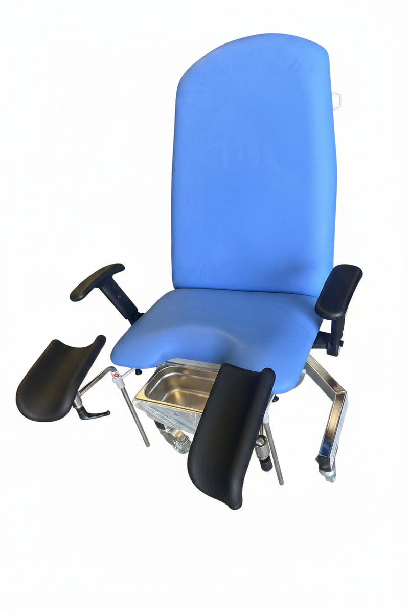 A blue medical examination chair with black armrests and footrests, photographed in a warehouse or storage area with concrete floors and other equipment visible in the background.