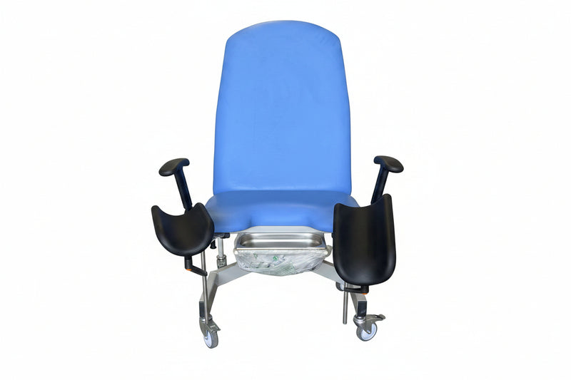 A blue medical examination chair with black armrests and a metal footrest tray, photographed in a warehouse or storage area with boxes and equipment in the background.