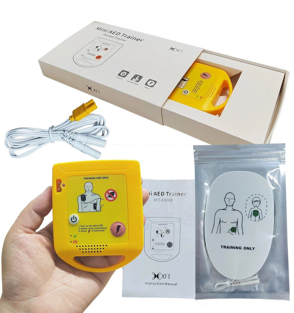 Yellow AED trainer with packaging, cable, and manual on a white background